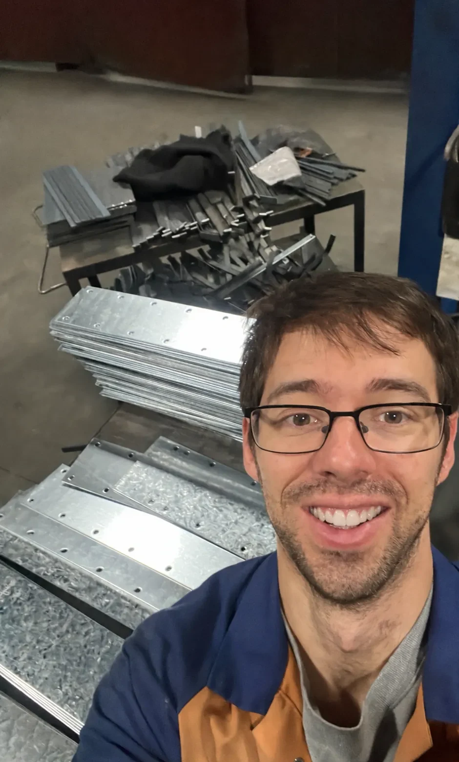 Stewart, the maker, smiling in the workshop beside a stack of new galvanised steel corner supports